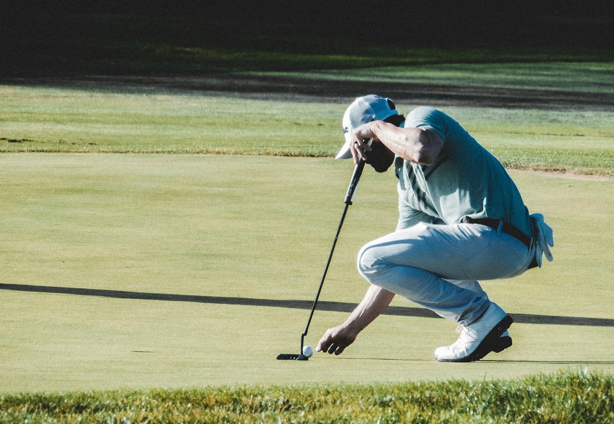 Joueur accroupi sur un green qui observe la pente avant de putter